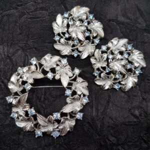 Demi parure anni ‘50 firmata Lisner, composta da spilla e orecchini a clip, decoro floreale, in metallo color argento con cristalli acquamarina - VINTAGE AMOREMIO